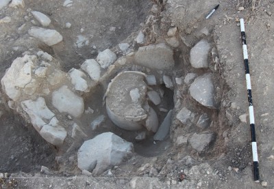Figure 6. A bin built up against an Iron Age wall, lined with clay and a recycled grinding stone; the bin contains a large, reconstructable vessel.